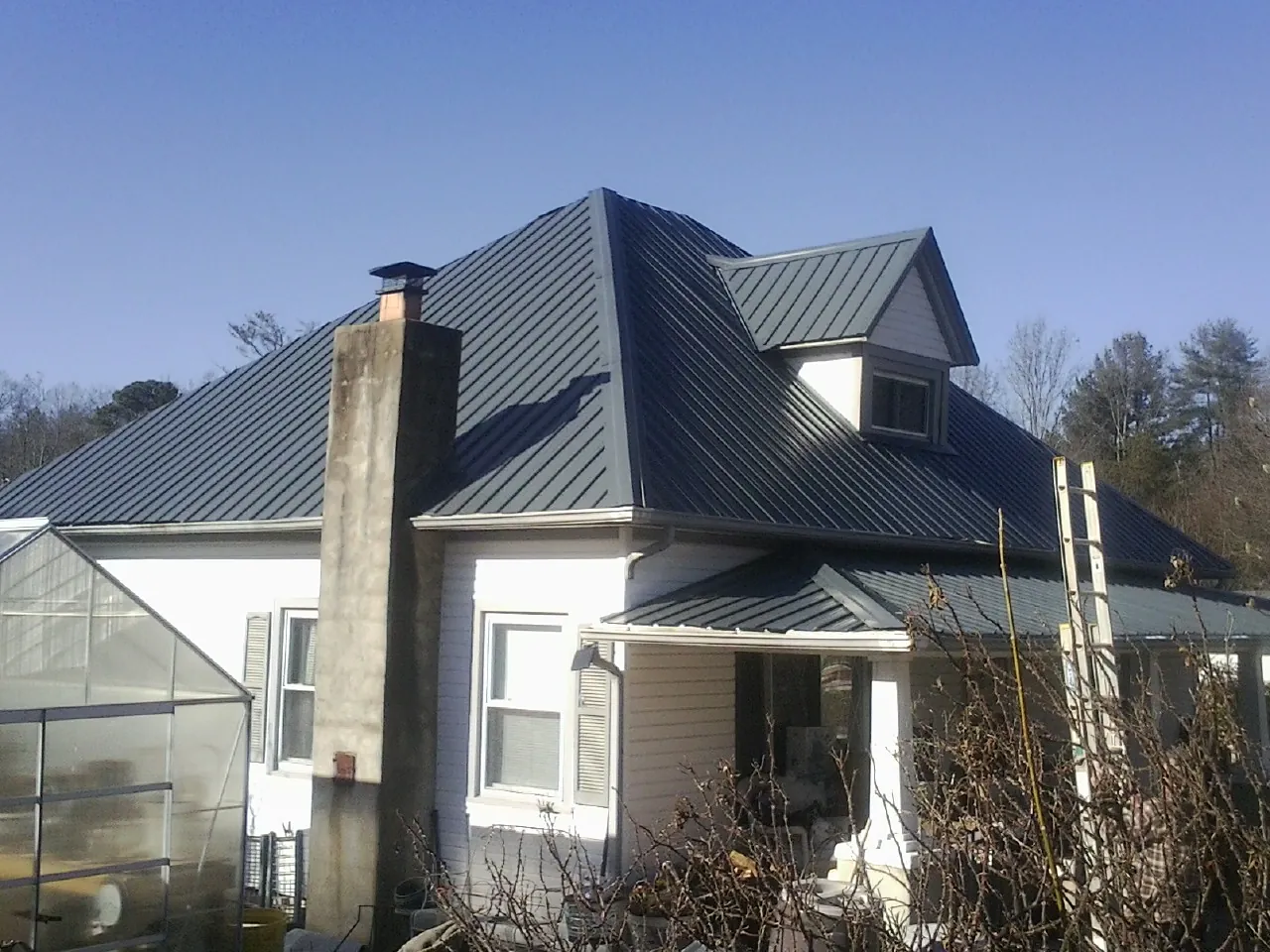 Dark blue standing seam metal roof on a white farmhouse with dormer — Slate & Tile Roof Repair by Roofing Brothers in Paonia