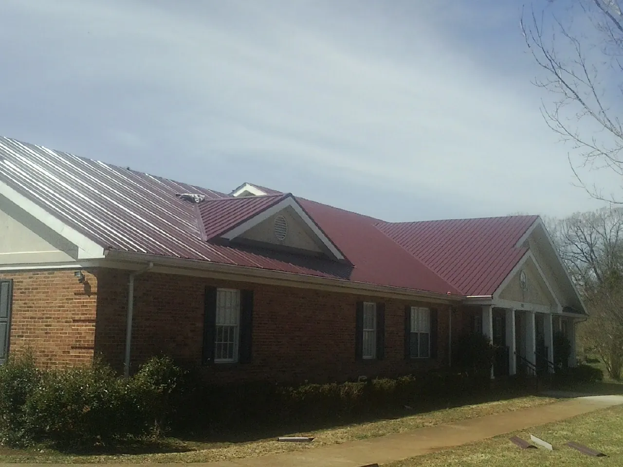 Red metal roof with gabled entries on a long brick building, from a Hail Damage Roof Repair job in Paonia