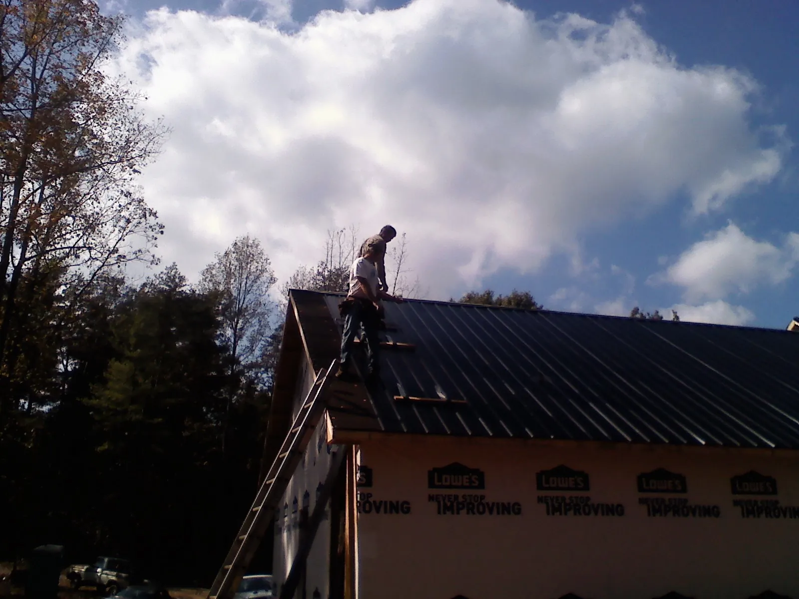 Roofer fastening dark metal panels high against a cloudy sky, from a Roof Inspection job in Paonia