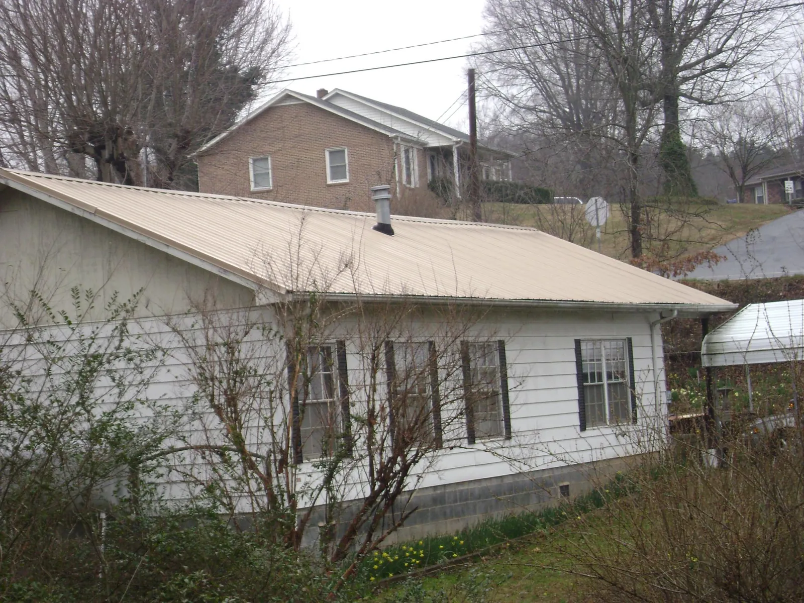 Tan metal roof on a white sided house set into a hillside — Commercial Roofing by Roofing Brothers in Paonia